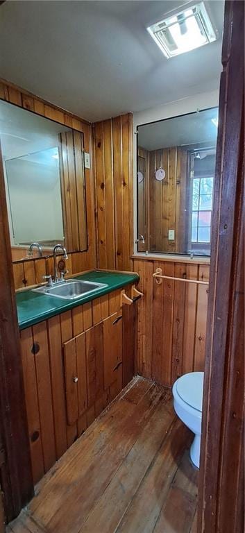 bathroom with hardwood / wood-style floors, toilet, vanity, and wooden walls