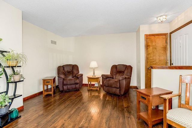 living area with visible vents, baseboards, a textured ceiling, and hardwood / wood-style flooring