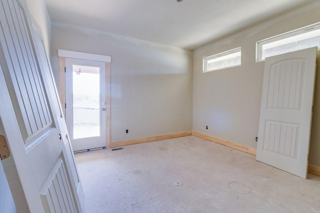 empty room with baseboards, plenty of natural light, and unfinished concrete flooring