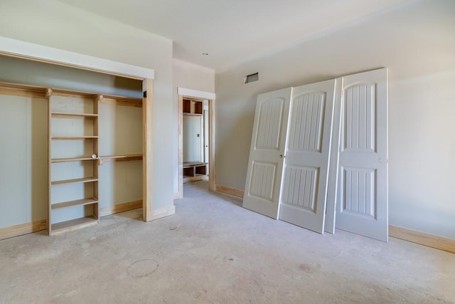 unfurnished bedroom with concrete flooring, a closet, and baseboards