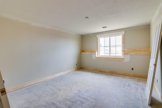 spare room featuring unfinished concrete flooring, visible vents, and baseboards