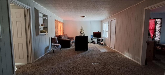 corridor with built in shelves, wood walls, crown molding, and carpet floors