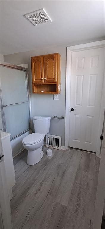 bathroom featuring combined bath / shower with glass door, hardwood / wood-style flooring, and toilet