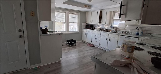 kitchen with light hardwood / wood-style floors, white cabinets, sink, a raised ceiling, and light stone counters