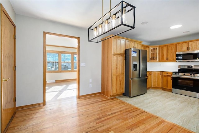 kitchen with appliances with stainless steel finishes, decorative light fixtures, and light wood-type flooring