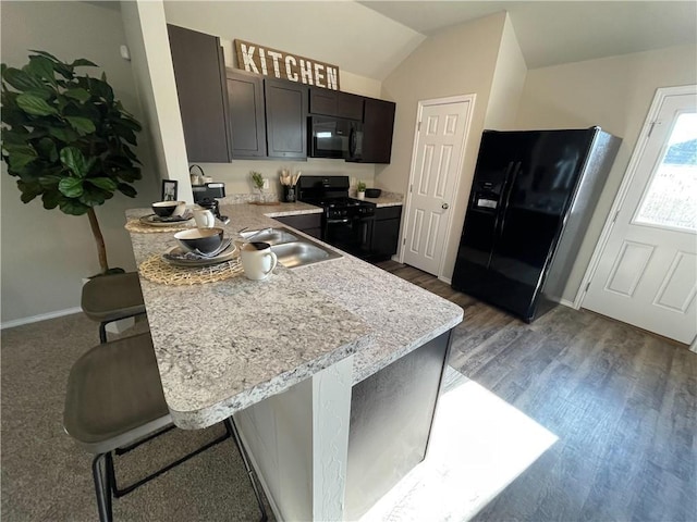 kitchen with black appliances, a kitchen breakfast bar, kitchen peninsula, light hardwood / wood-style flooring, and vaulted ceiling