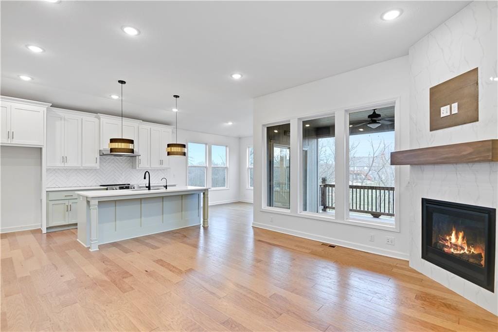 kitchen with a tile fireplace, white cabinetry, hanging light fixtures, a kitchen island with sink, and light wood-type flooring