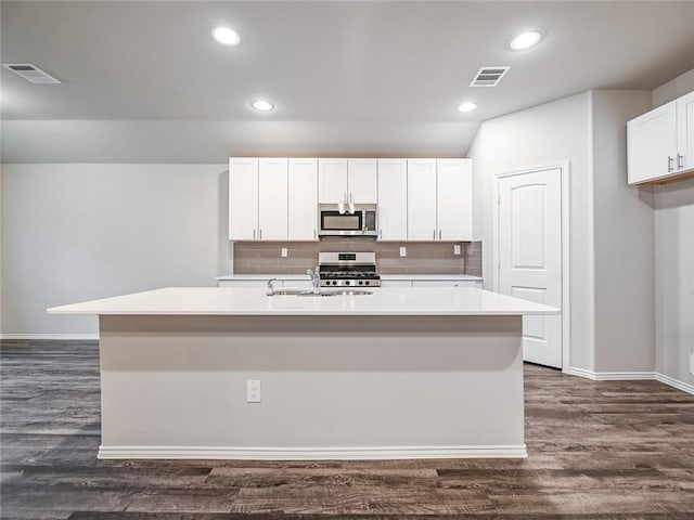 kitchen with white cabinets, backsplash, stainless steel appliances, a center island with sink, and dark hardwood / wood-style floors