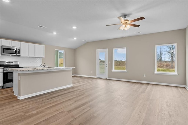 kitchen featuring light stone countertops, white cabinets, appliances with stainless steel finishes, decorative backsplash, and a kitchen island with sink