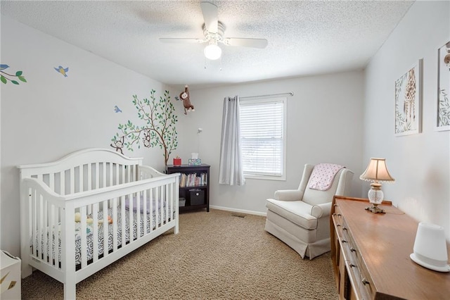 carpeted bedroom with a crib, a textured ceiling, and ceiling fan