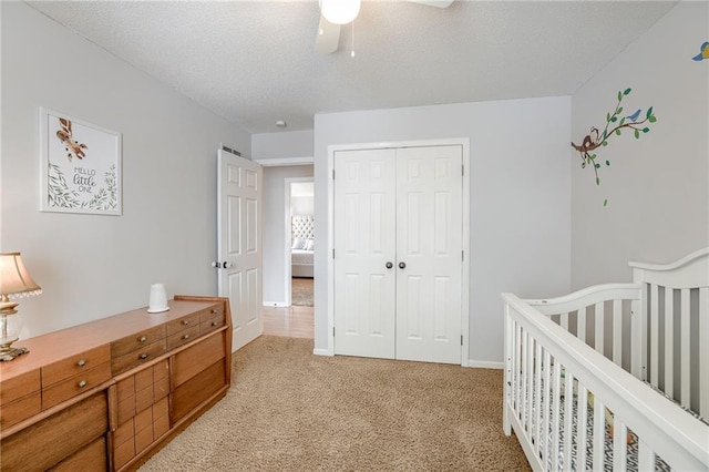 carpeted bedroom with a crib, ceiling fan, and a closet