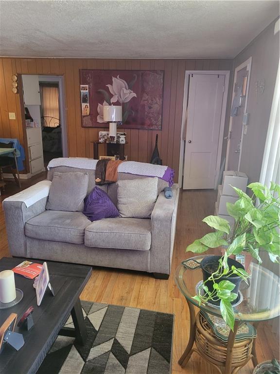 living room with hardwood / wood-style flooring, wooden walls, and a textured ceiling