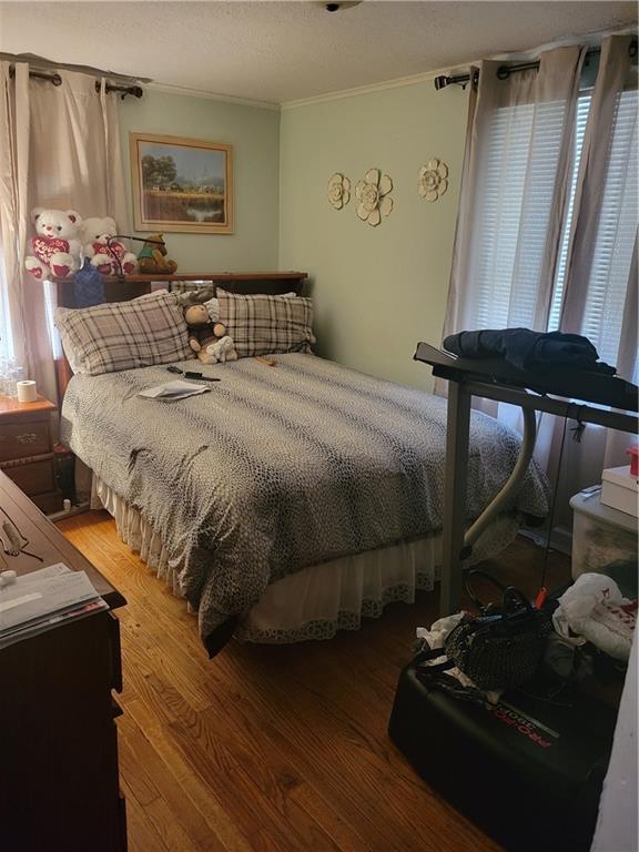 bedroom featuring hardwood / wood-style flooring, crown molding, multiple windows, and a textured ceiling