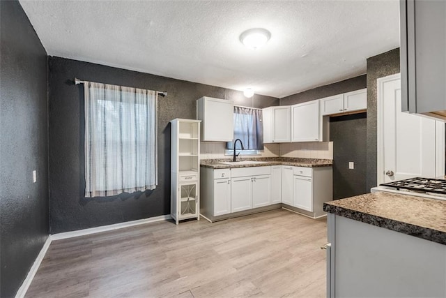 kitchen featuring white cabinetry, sink, light hardwood / wood-style flooring, and a textured ceiling