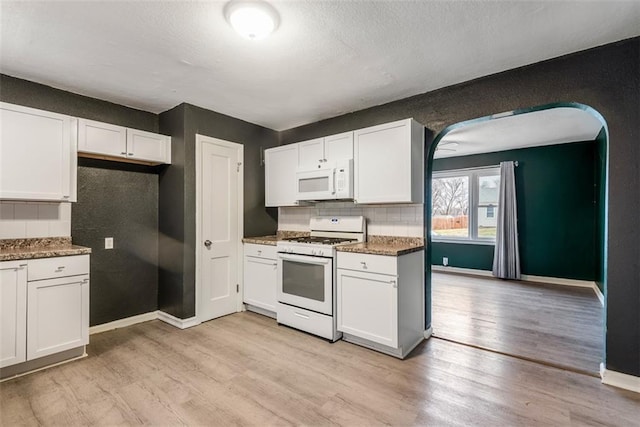 kitchen featuring white appliances, dark stone counters, light hardwood / wood-style flooring, and white cabinets