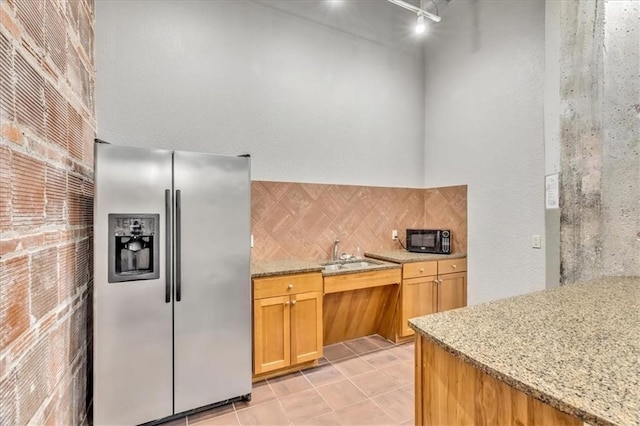 kitchen with black microwave, a sink, light stone countertops, tasteful backsplash, and stainless steel fridge