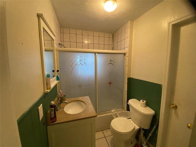 full bathroom featuring bath / shower combo with glass door, tile patterned flooring, vanity, toilet, and a textured ceiling