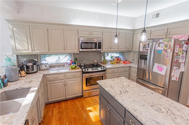 kitchen with light hardwood / wood-style floors, appliances with stainless steel finishes, hanging light fixtures, sink, and gray cabinets