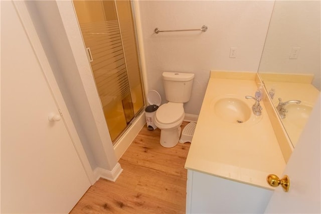 bathroom with wood-type flooring, a shower with door, toilet, and vanity