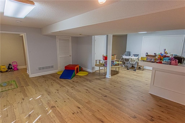 game room featuring light wood-type flooring and a textured ceiling