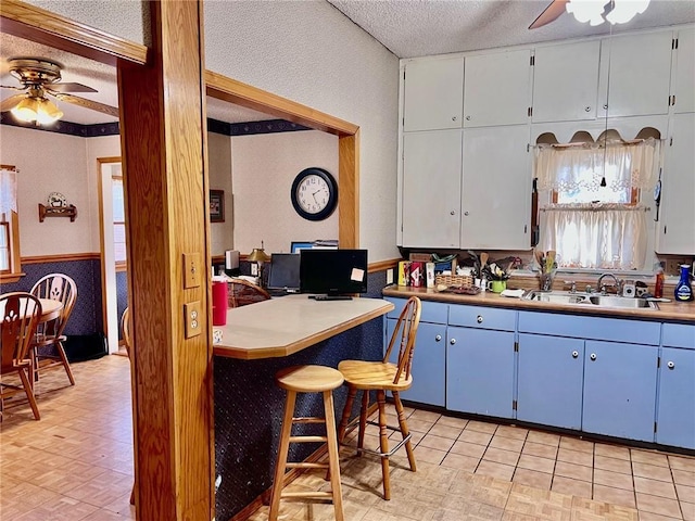 kitchen featuring ceiling fan, sink, blue cabinetry, beam ceiling, and a textured ceiling