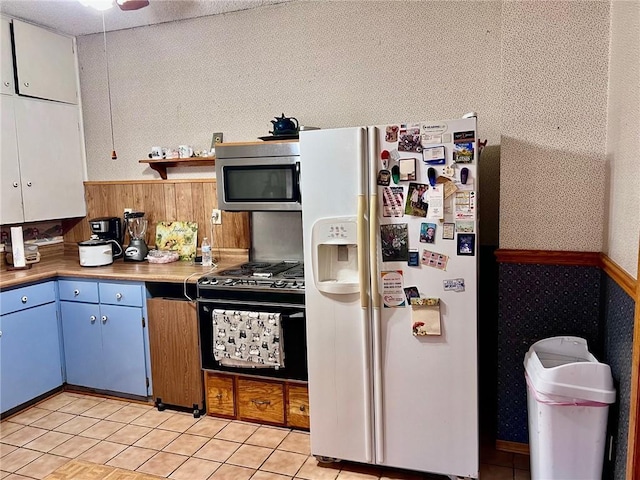 kitchen with white fridge with ice dispenser, wooden walls, black gas range oven, blue cabinets, and light tile patterned flooring