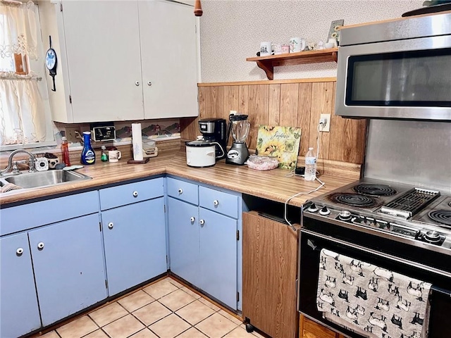 kitchen with wooden walls, black range with electric cooktop, sink, blue cabinetry, and light tile patterned floors