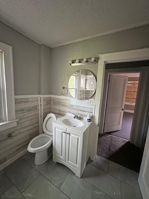 3920 S Benton Ave, Kansas City, MO 64130 - bathroom featuring a textured ceiling, a wainscoted wall, marble finish flooring, vanity, and toilet