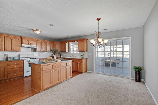 kitchen with hanging light fixtures, a center island, a notable chandelier, light colored carpet, and white gas stove