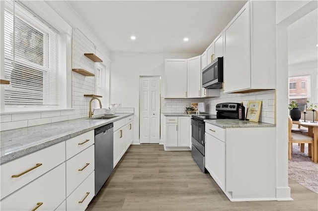 kitchen with light wood finished floors, open shelves, appliances with stainless steel finishes, a sink, and light stone countertops