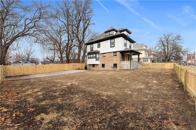 rear view of house with stone siding and a fenced backyard