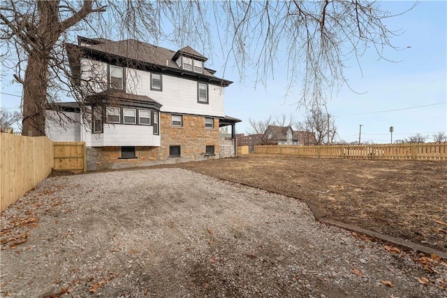 rear view of property featuring stone siding, a fenced backyard, and driveway