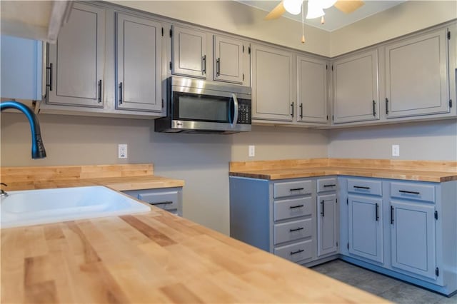 kitchen with gray cabinets, butcher block counters, sink, light tile patterned floors, and ceiling fan