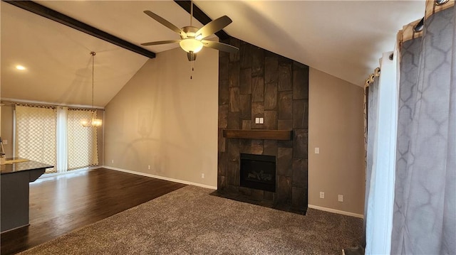 unfurnished living room with ceiling fan, beam ceiling, high vaulted ceiling, a fireplace, and dark carpet