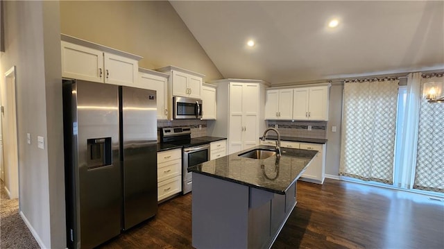 kitchen featuring appliances with stainless steel finishes, white cabinetry, sink, dark stone countertops, and a kitchen island with sink