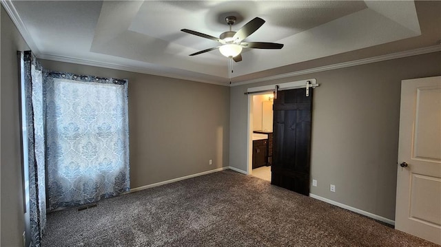 unfurnished bedroom with a tray ceiling, ornamental molding, a barn door, and carpet flooring