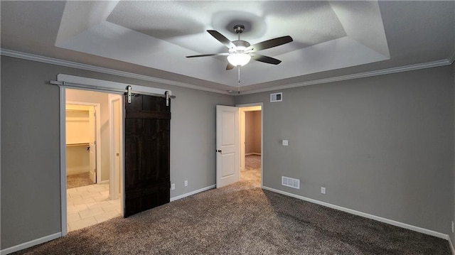 unfurnished bedroom with carpet flooring, ornamental molding, ceiling fan, a raised ceiling, and a barn door