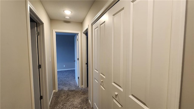 corridor with a textured ceiling and dark colored carpet