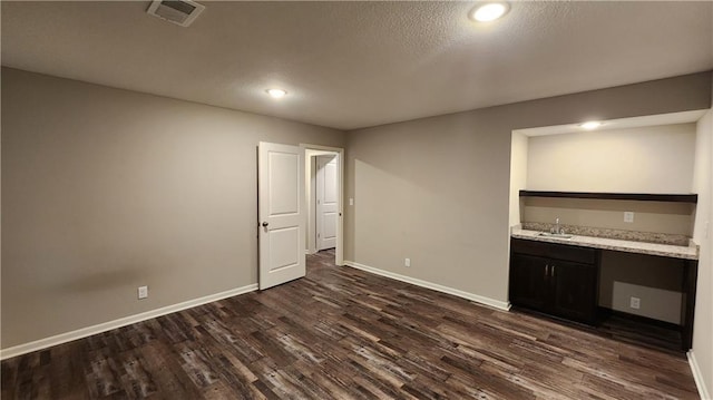 unfurnished bedroom featuring dark hardwood / wood-style flooring, sink, built in desk, and a textured ceiling