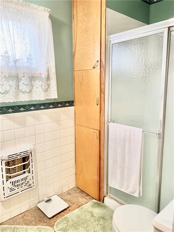 bathroom featuring toilet, heating unit, walk in shower, and tile walls