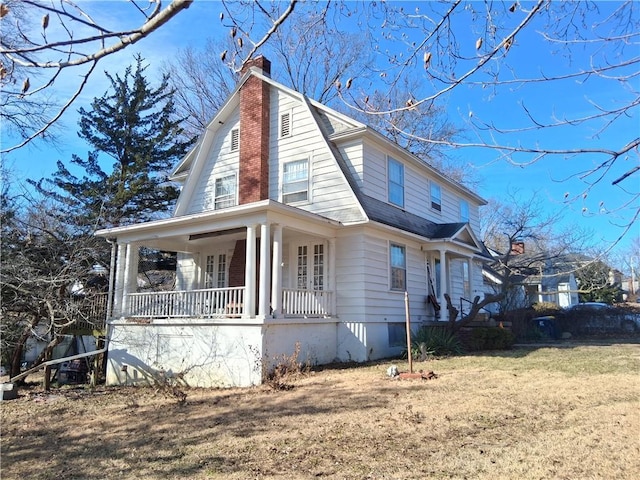 view of side of home featuring a chimney, a porch, a shingled roof, a lawn, and a gambrel roof