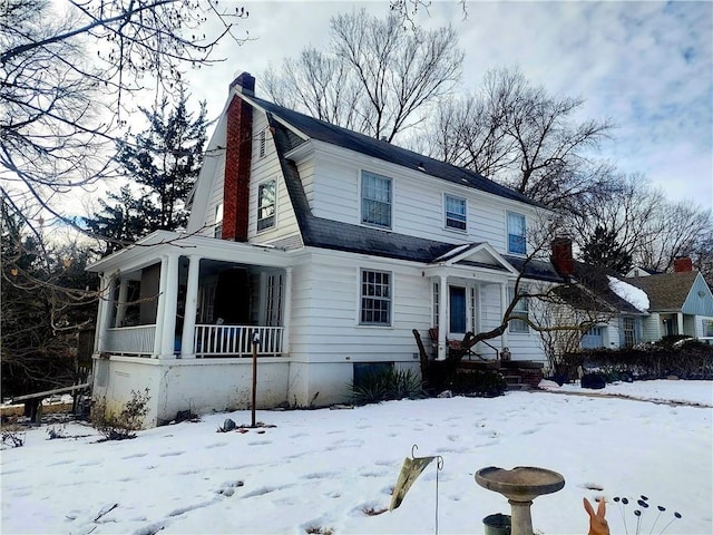 dutch colonial featuring roof with shingles, a porch, a chimney, and a gambrel roof