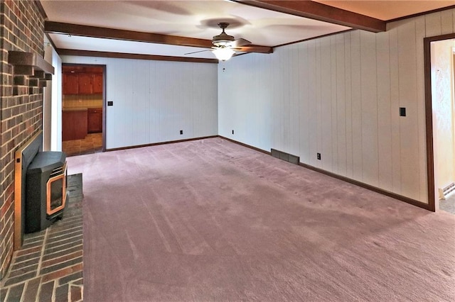 unfurnished living room with ceiling fan, beam ceiling, carpet, and a wood stove