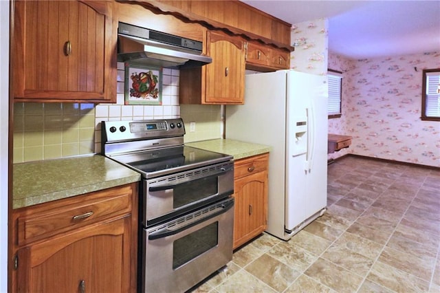 kitchen with brown cabinetry, double oven range, wallpapered walls, white fridge with ice dispenser, and under cabinet range hood