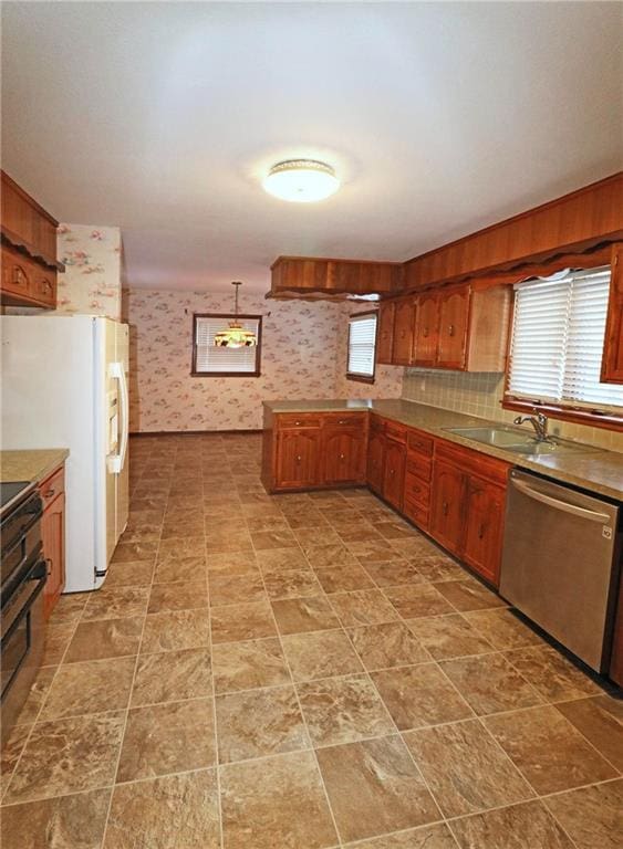 kitchen with a sink, stainless steel dishwasher, freestanding refrigerator, a peninsula, and wallpapered walls