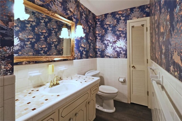 bathroom with vanity, a wainscoted wall, wallpapered walls, tile walls, and toilet