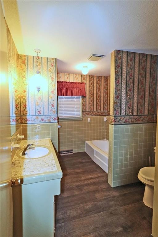 bathroom featuring wood finished floors, a wainscoted wall, wallpapered walls, tile walls, and a bath