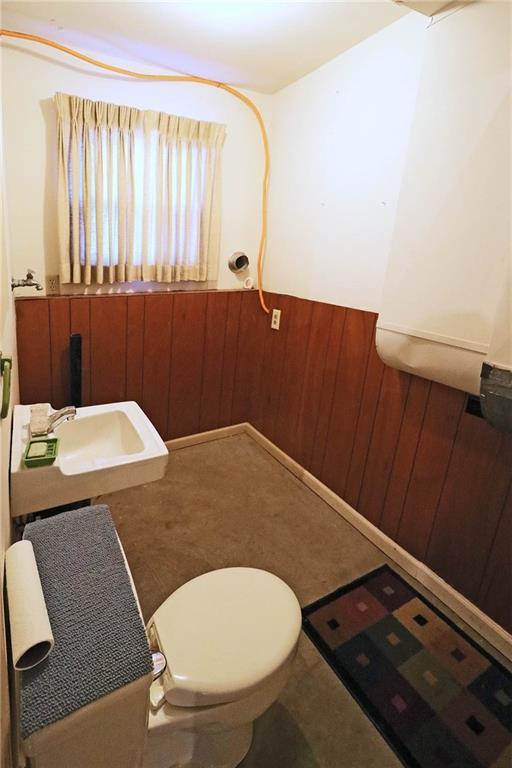 bathroom featuring wooden walls, toilet, a wainscoted wall, and a sink