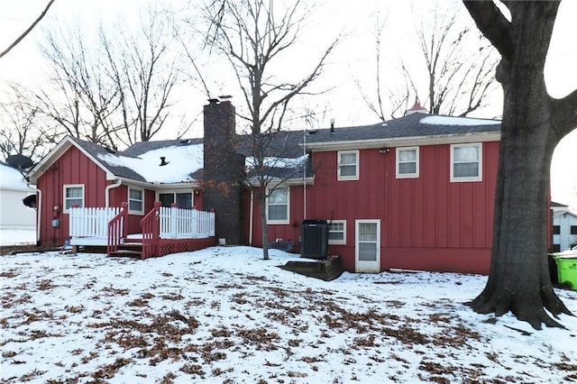 snow covered property featuring central air condition unit, board and batten siding, and a chimney