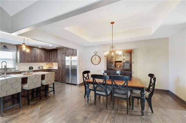 dining area with sink, hardwood / wood-style flooring, a notable chandelier, and a raised ceiling